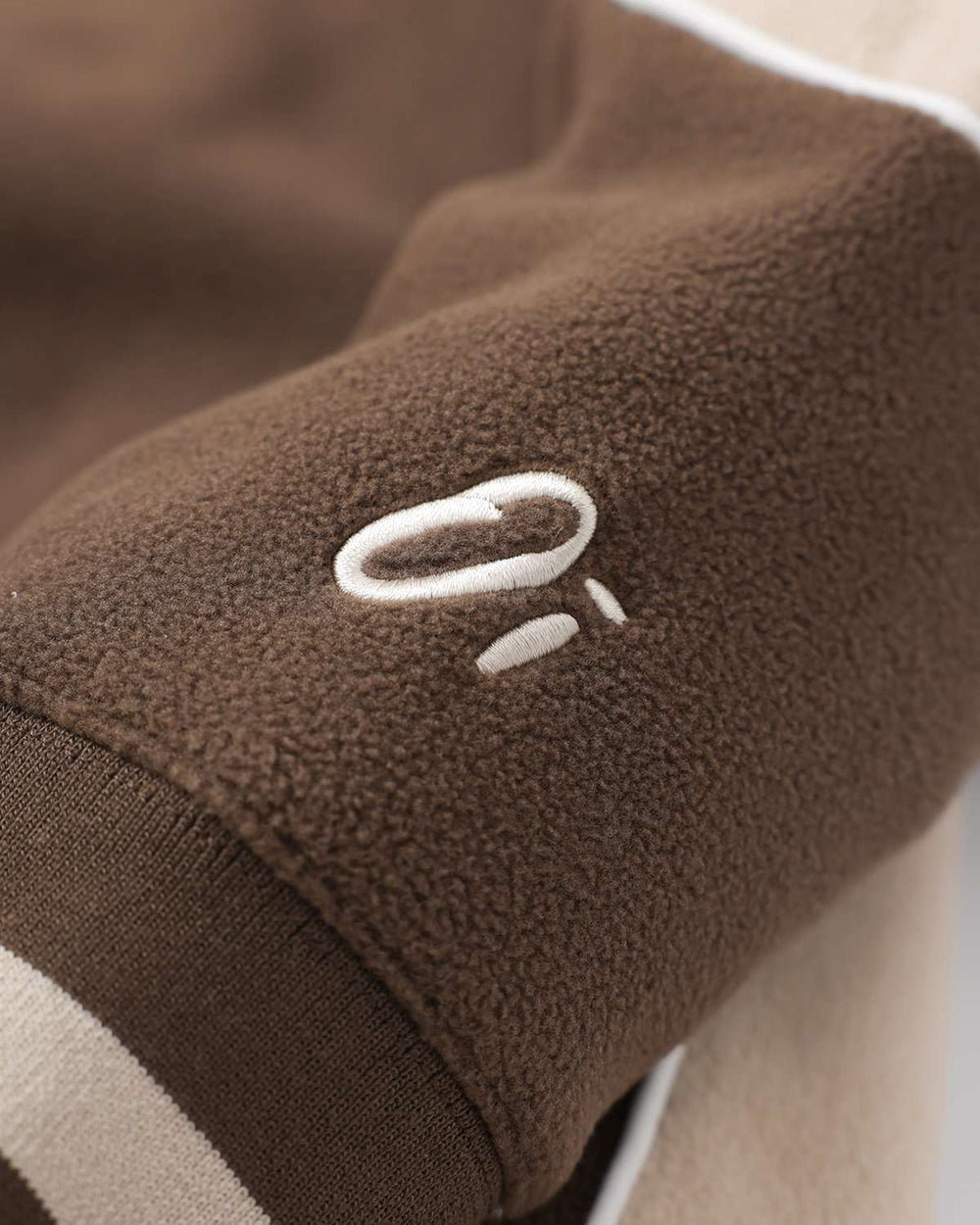 Brown fleece sleeve with white logo patch and ribbed cuff with contrast stripe