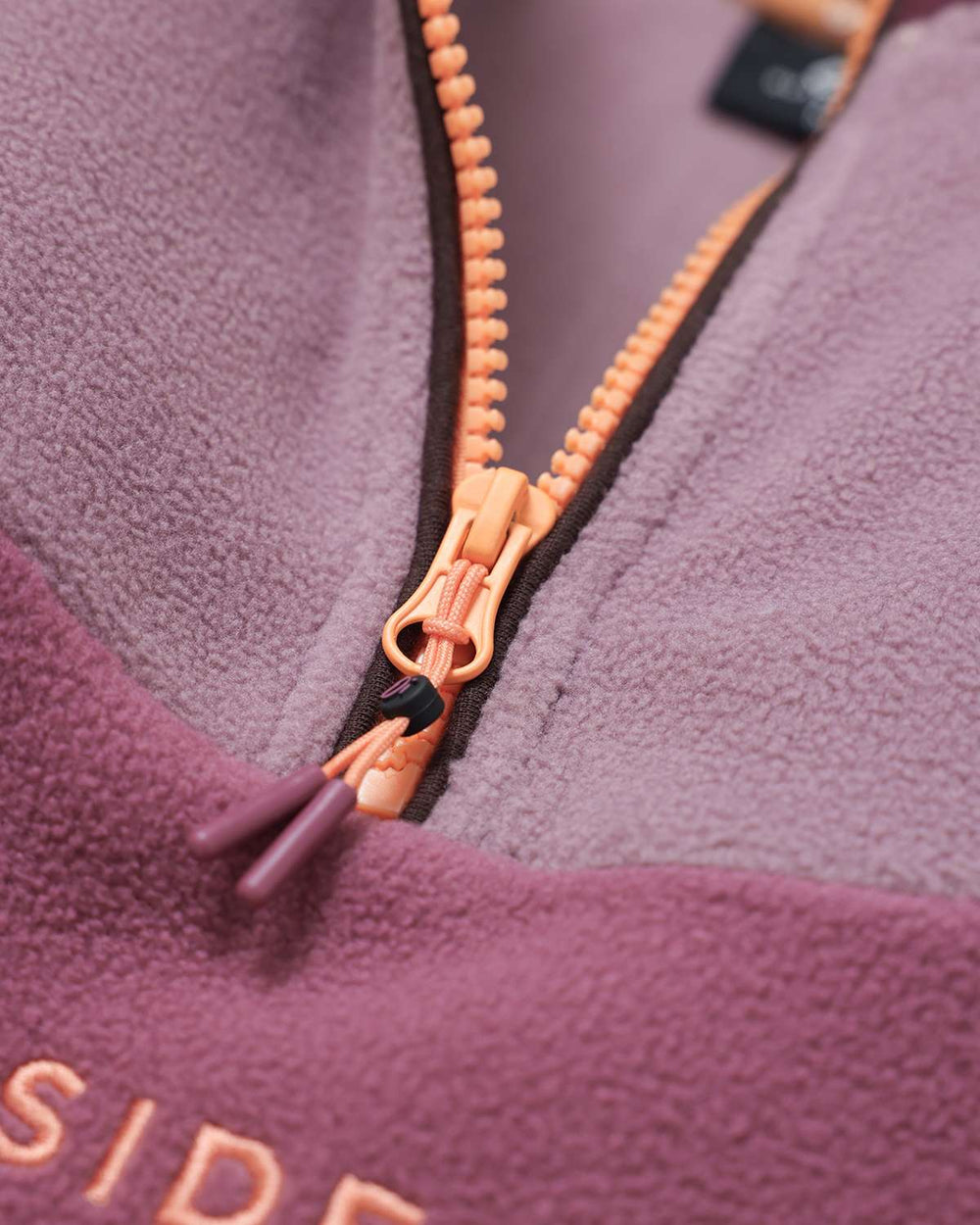 Quarter-zip fleece zipper with orange-gold pull on burgundy and mauve fabric