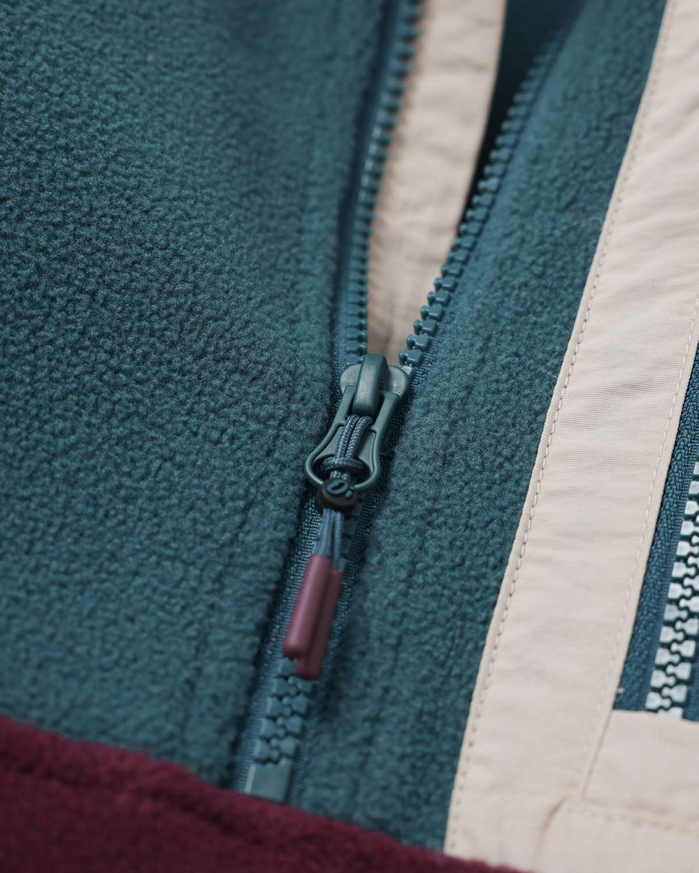 Close-up of microfleece zipper with fabric pull tabs on teal and white color-block panel