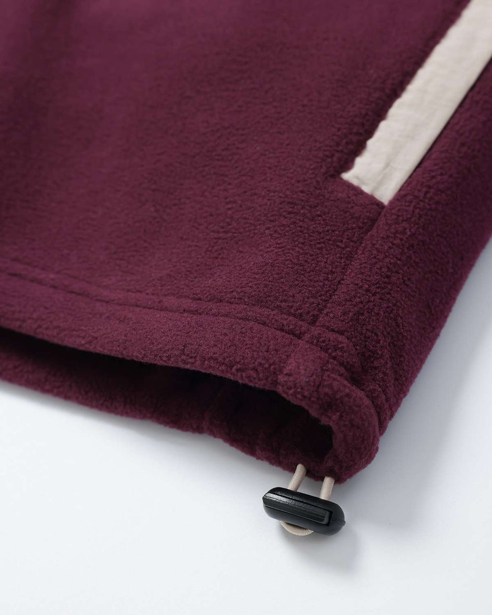Bottom hem of maroon microfleece jacket with fabric pull cord stopper and stitched edge