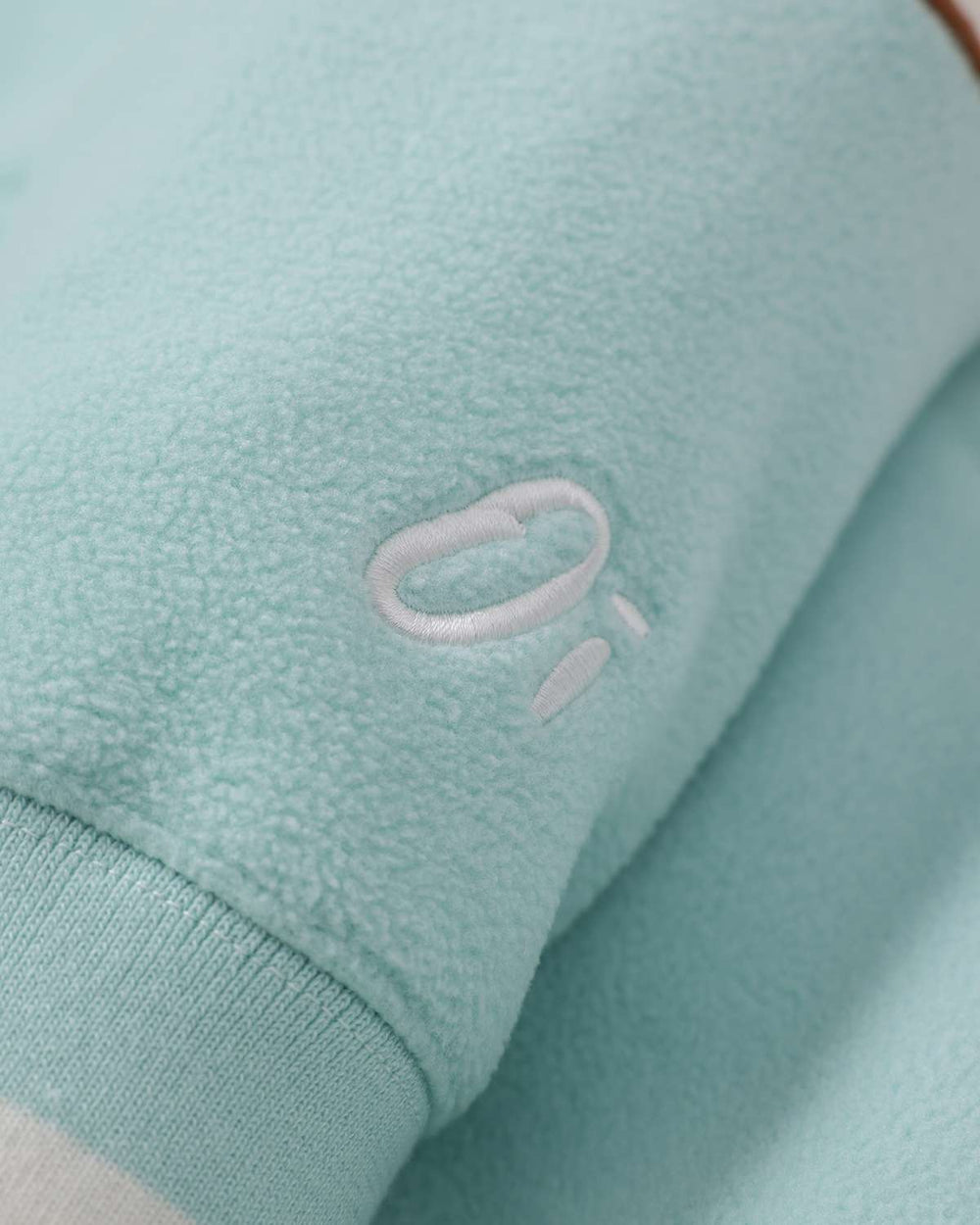 Light teal fleece fabric with oval logo patch near the sleeve cuff and ribbed edge