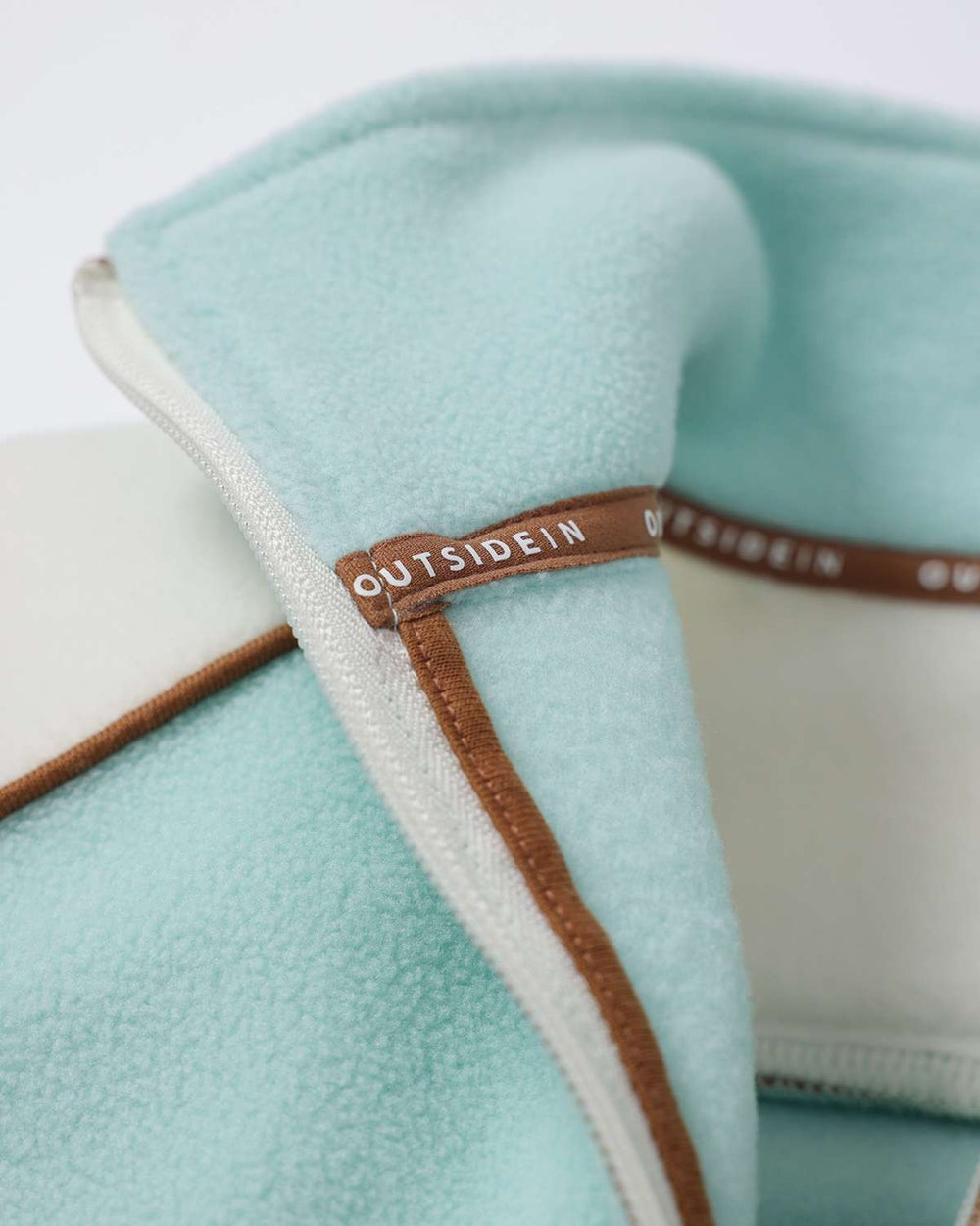 Light teal fleece zipper area with brown trim and white cord detail at collar