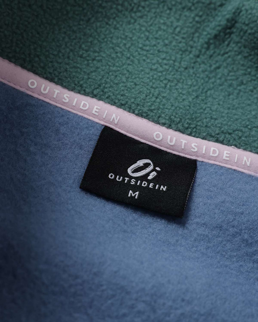 Fleece jacket interior brand label on blue panel with pink logo tape and green trim