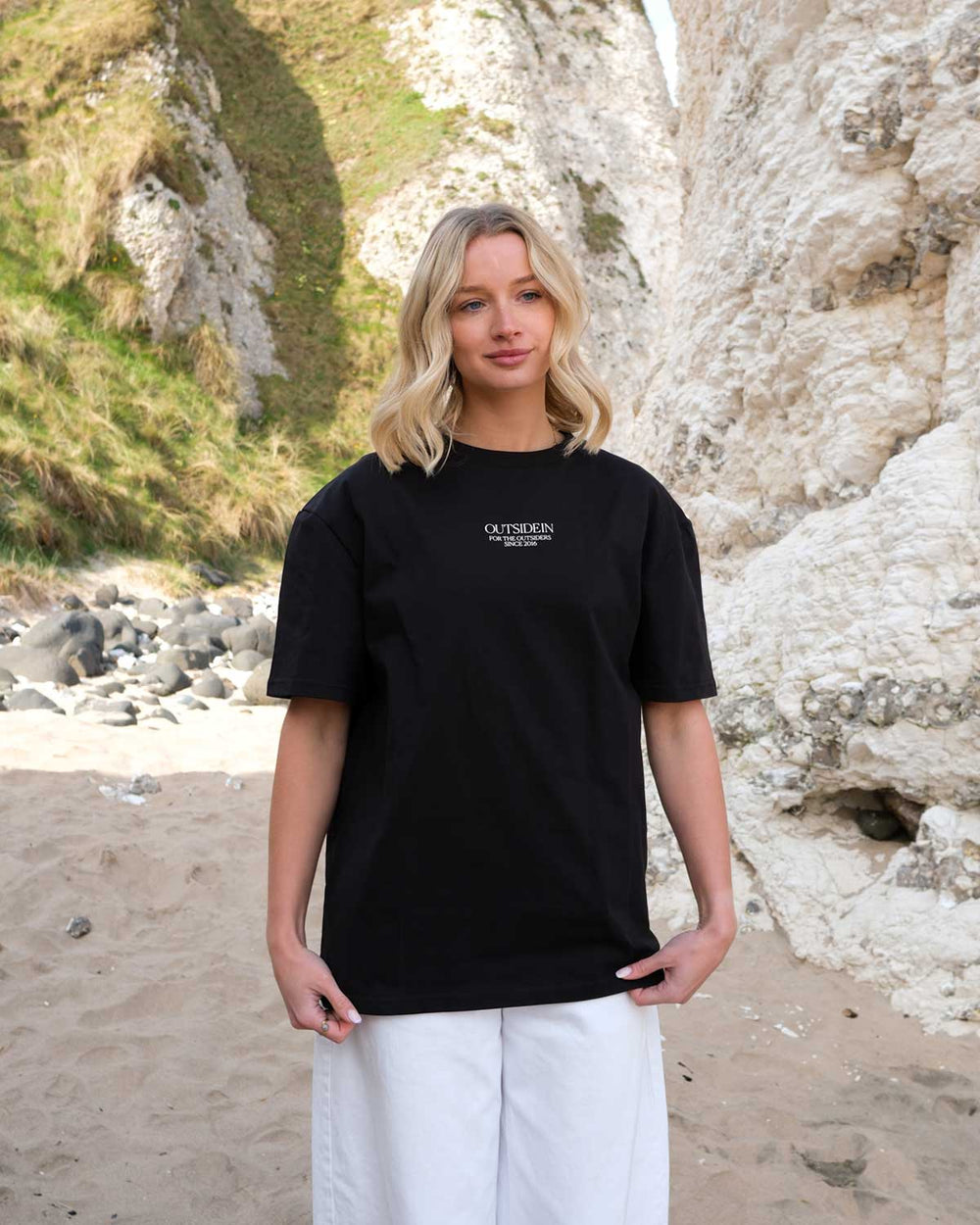 Model wearing an OutsideIn Black Abstract Causeway T shirt on a beach