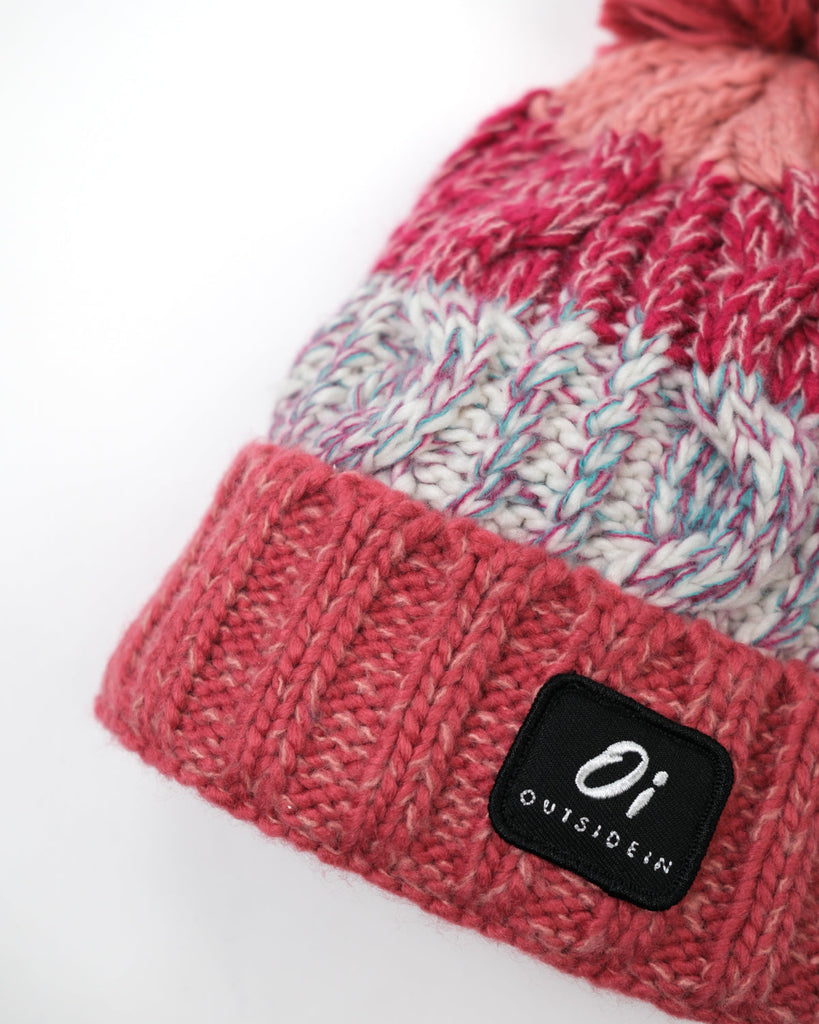 Pom hat in Coral Reef colour with classic cable knit pattern and partial fleece base lining