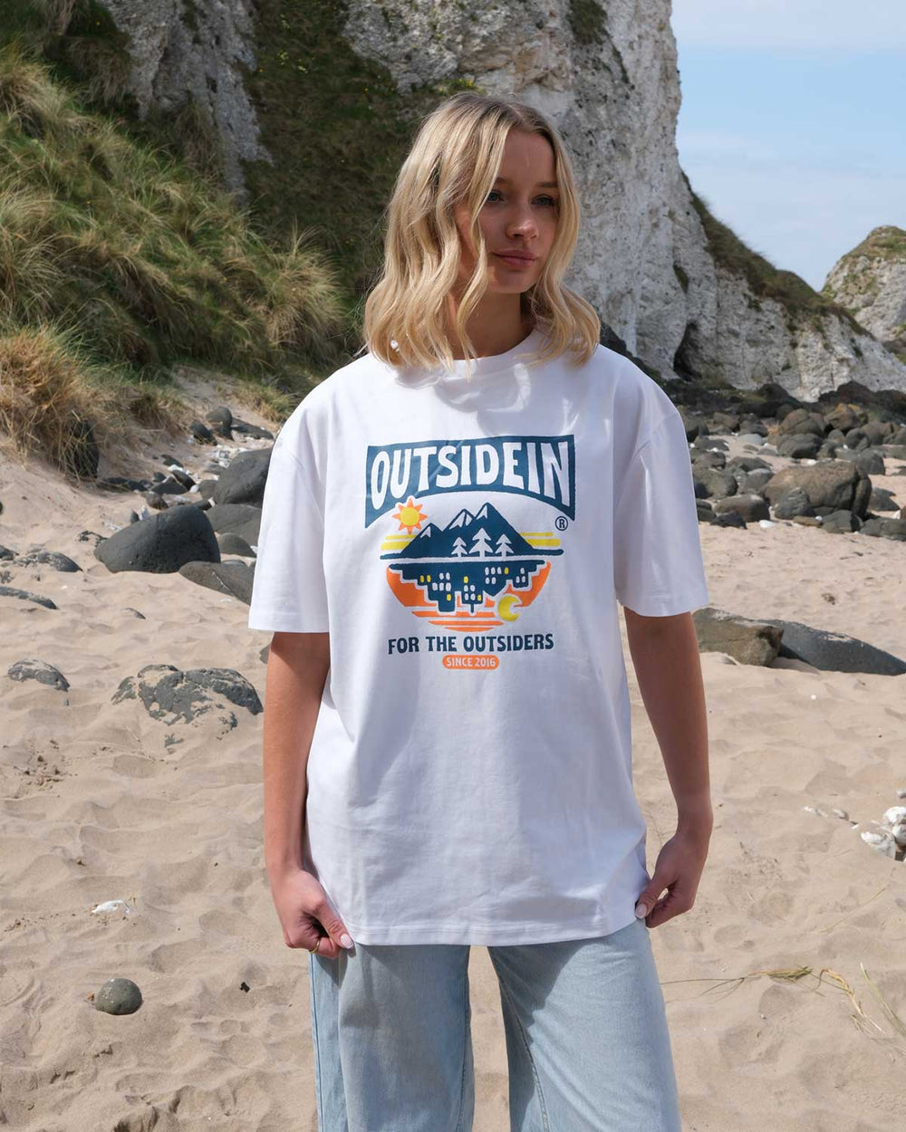 Model wearing a white t-shirt with 'OUTSIDEIN' logo on a beach