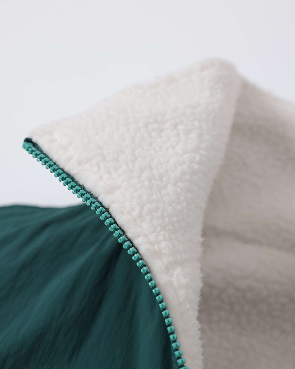 Reversible jacket close-up showing white fleece lining and teal zipper edge