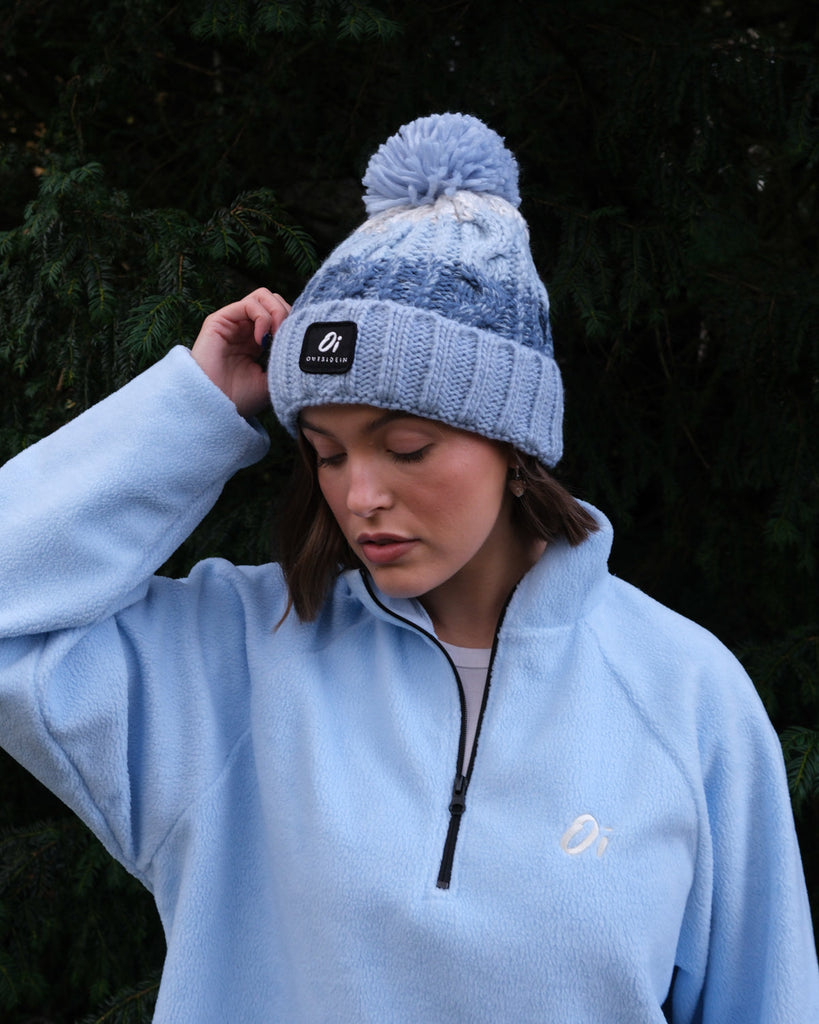 Pom hat with Arctic Breeze blue hues, cable knit design, and soft fleece-lined base