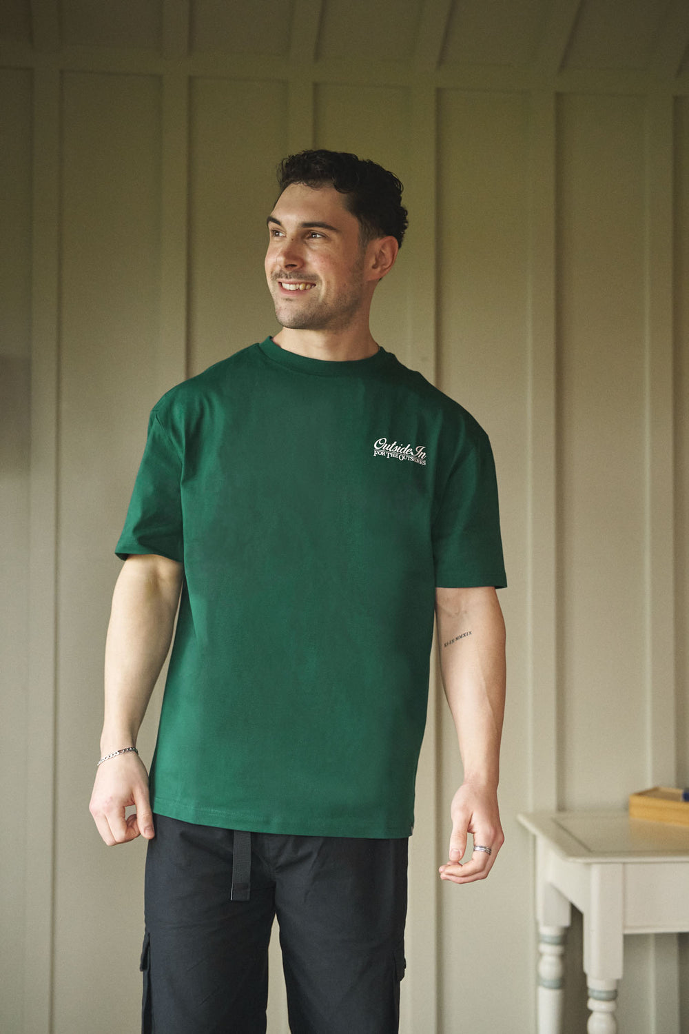 Model wearing a pine green t-shirt with 'OutsideIn' chest graphic.