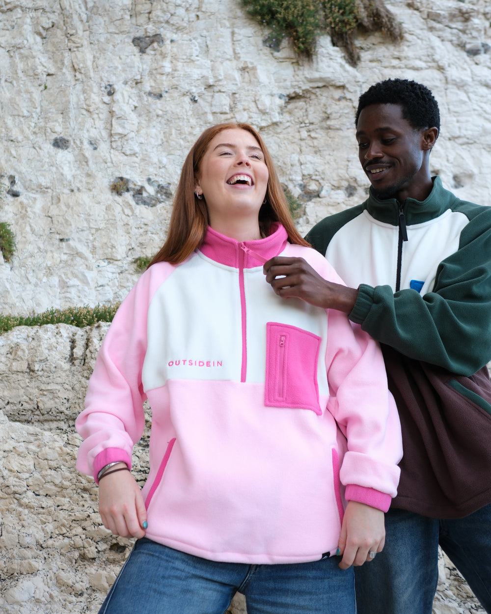A girl wearing a colour-blocked pink Half-zip fleece pullover by Outsidein, featuring a light pink body, a cream chest panel, and bright pink accents on the collar, zipper, chest pocket, and cuffs, shown against a light grey background.