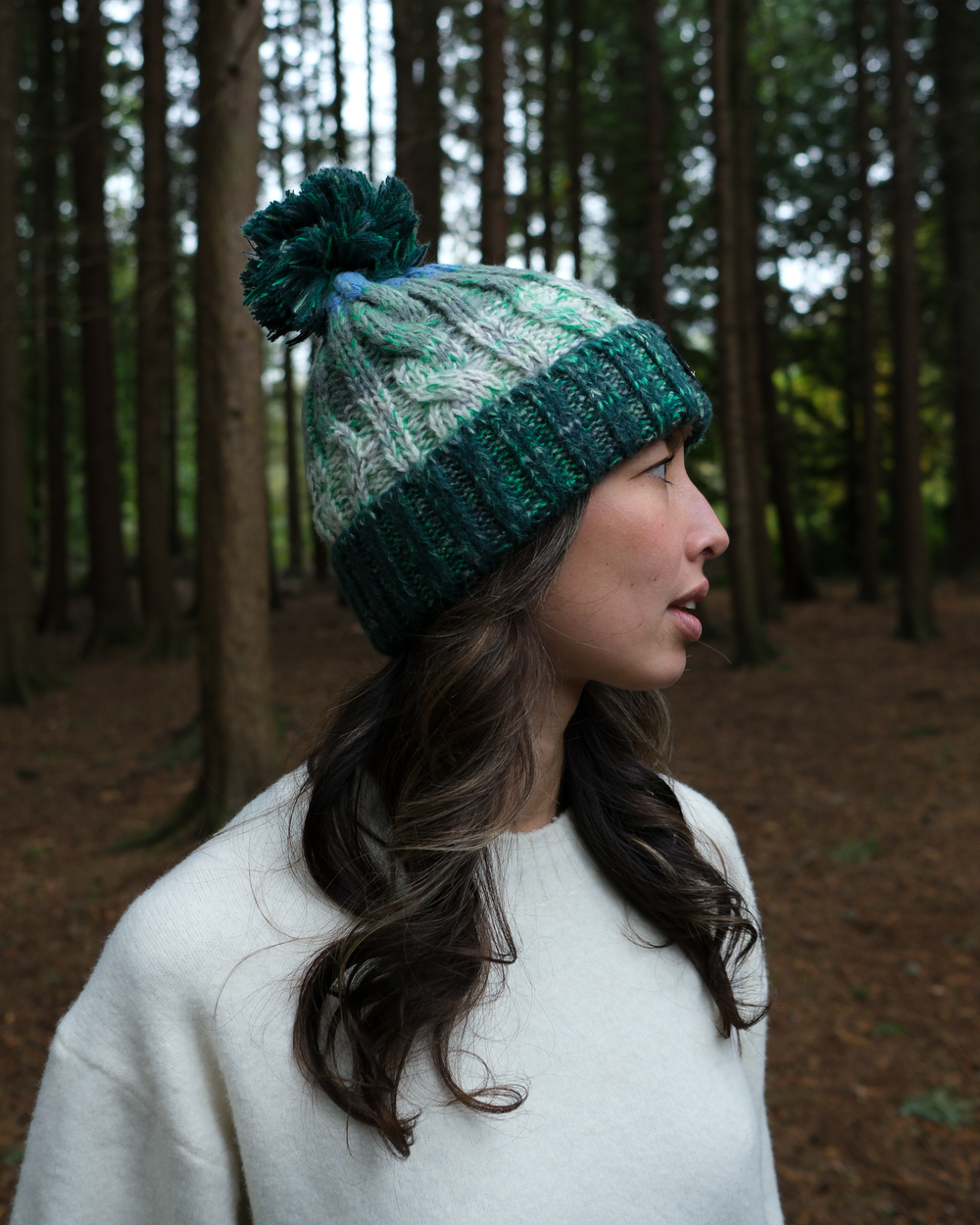 Two-tone knit beanie on model, with pom-pom and ribbed dark green cuff.