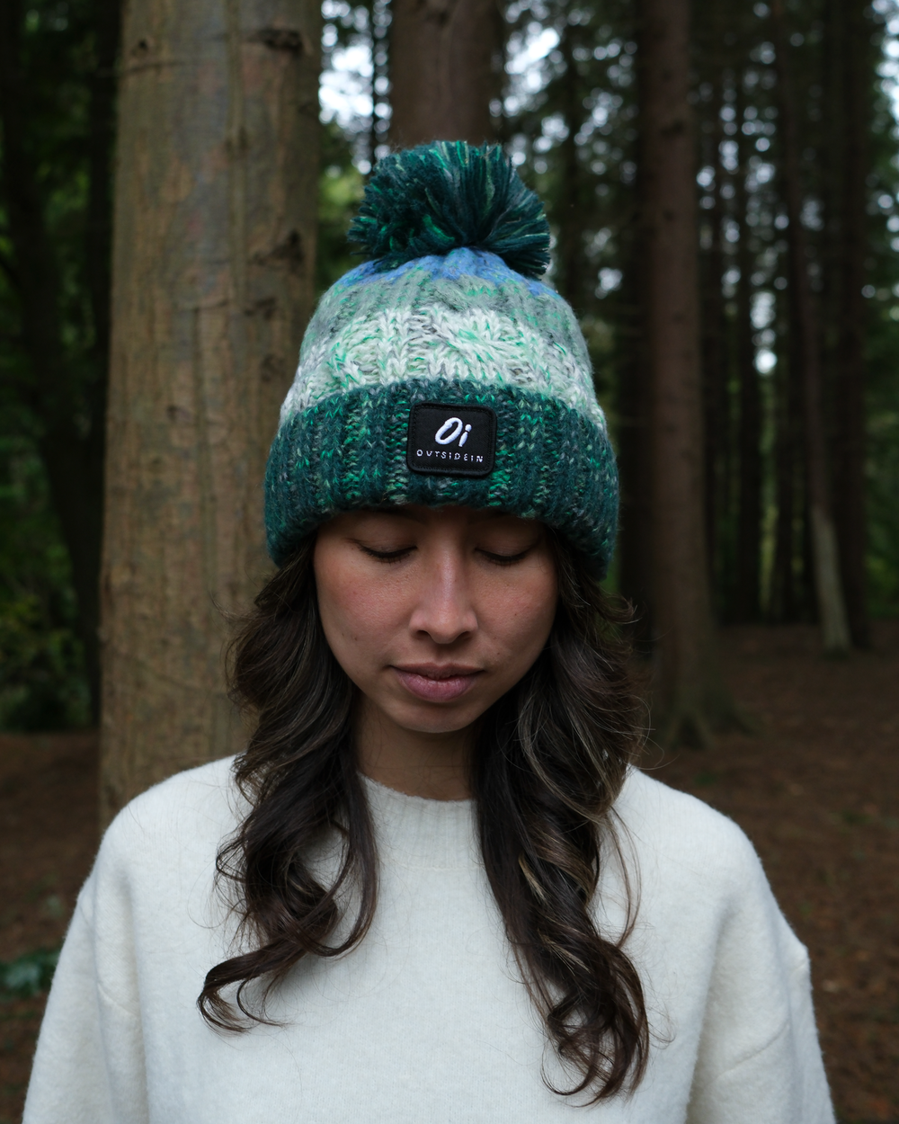 Two-tone knit beanie with pom-pom and front logo patch on dark green cuff.
