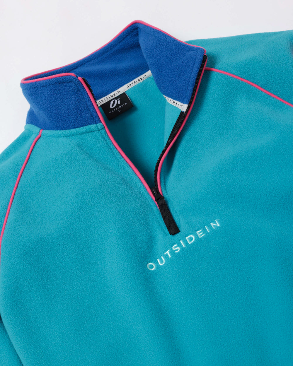 Close-up of a teal quarter-zip fleece pullover with a royal blue collar, pink piping, and white 'OUTSIDEIN' text on the chest.