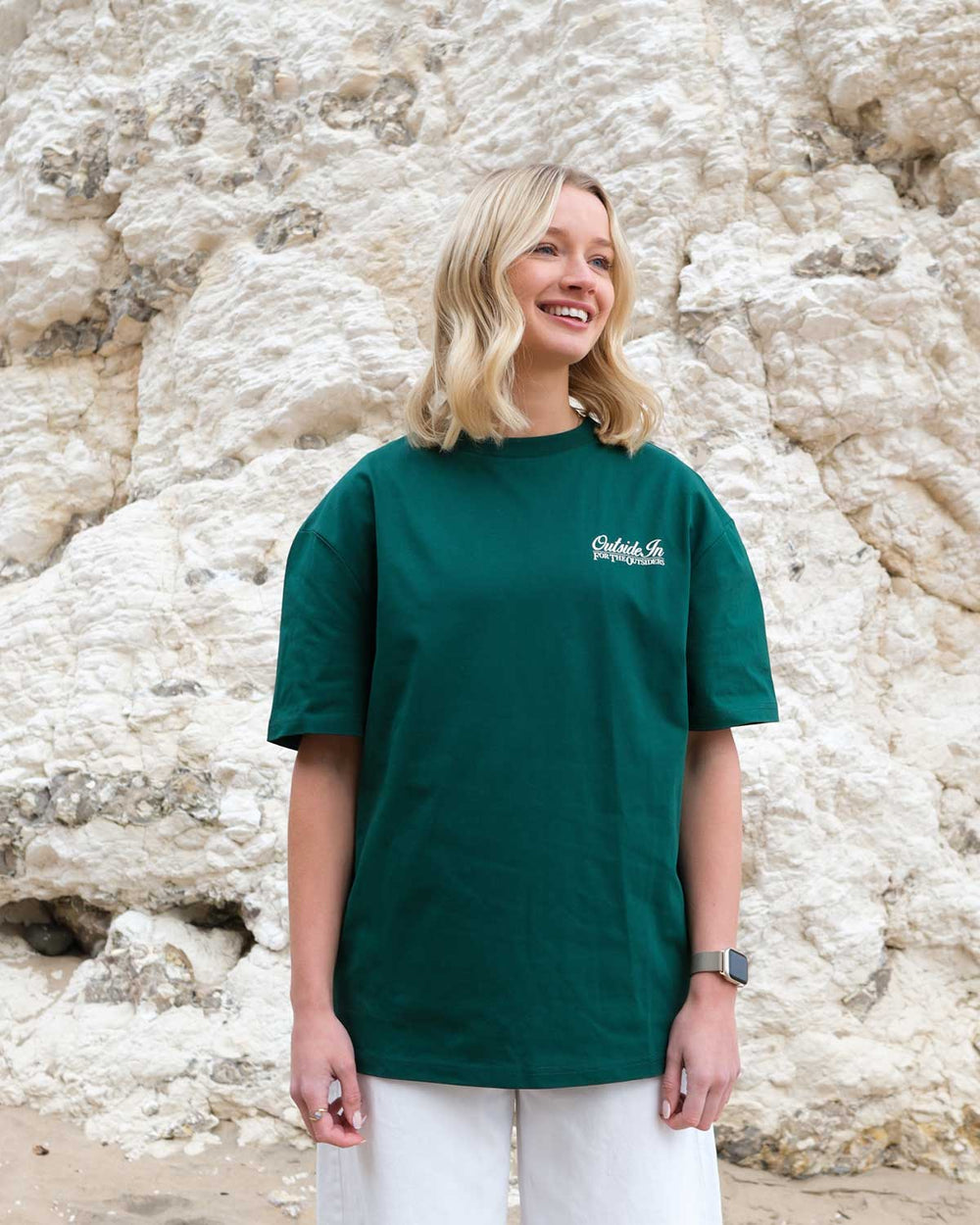 Model wearing OutsideIn Pine Green Whiterocks t-shirt against rocky background.