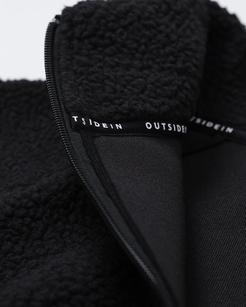 Close-up of a black essential fleece jacket with 'OUTSIDEIN' branding.